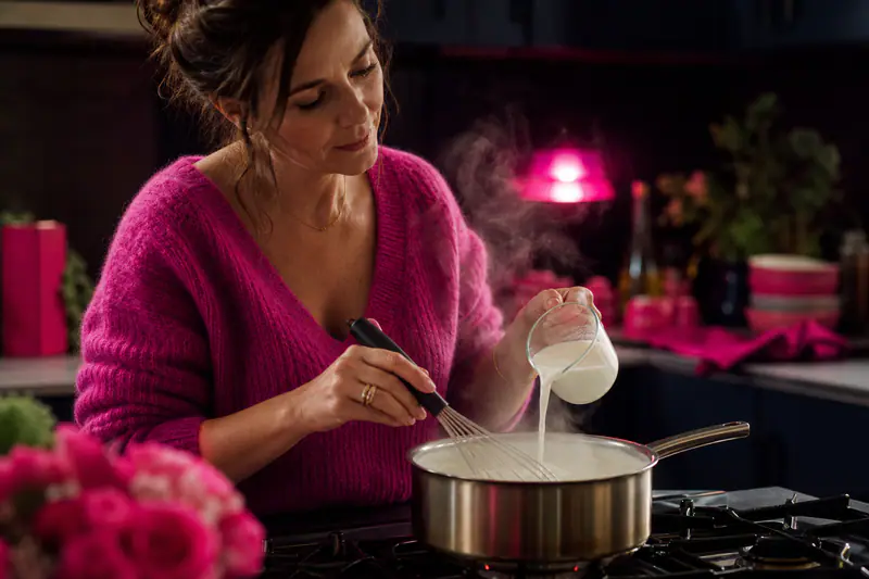 Femme fouettant une casserole de béchamel, filet de lait versé en cours de préparation