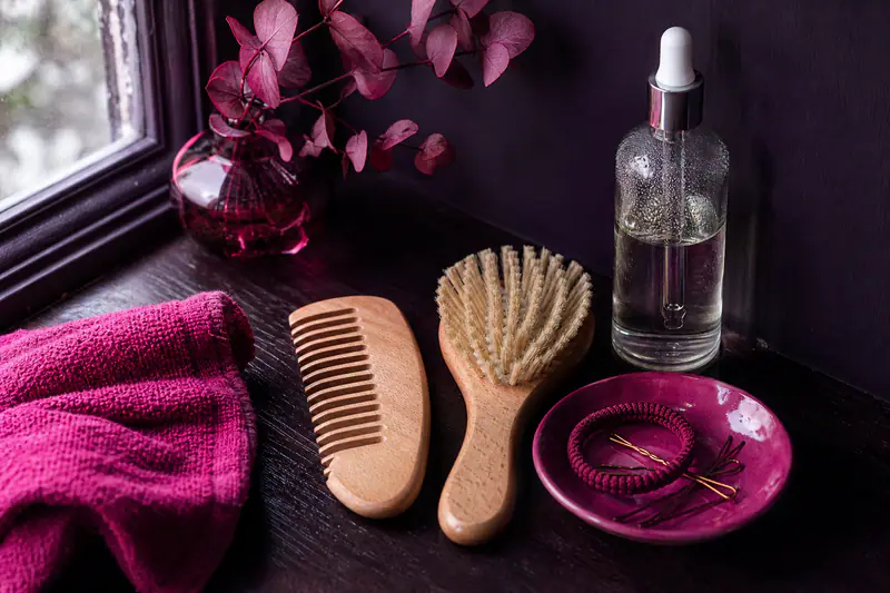 Peigne en bois, brosse et flacon d’huile capillaire sur une étagère sombre