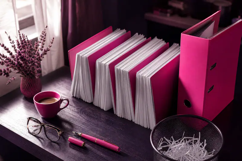 Piles de documents triées avec intercalaires roses et classeur sur un bureau sombre