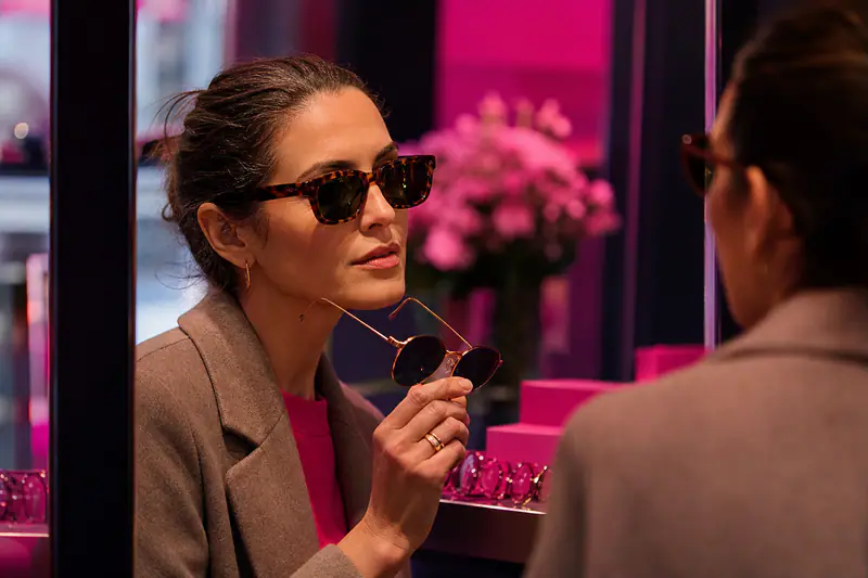 Femme essayant des lunettes de soleil adaptées devant un miroir d’opticien
