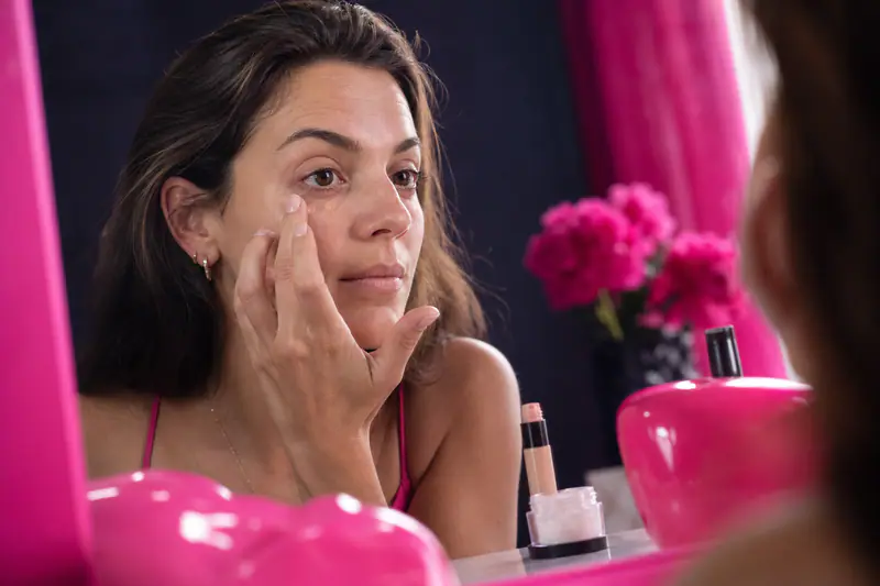 Femme appliquant un correcteur pêche sous l’œil devant une fenêtre
