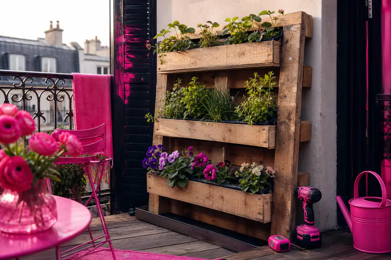 Palette recyclée verticale avec trois jardinières d’aromatiques sur un balcon
