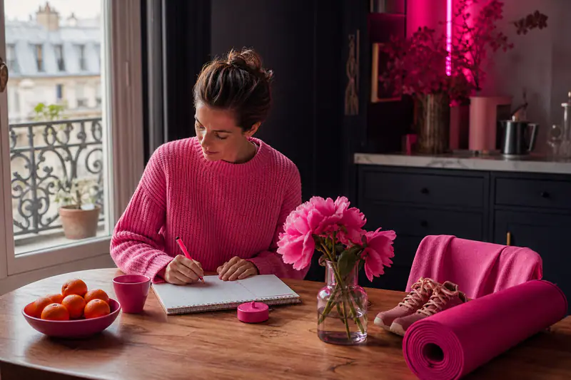 Femme organisant calmement ses objectifs hivernaux avec carnet, thé et baskets.