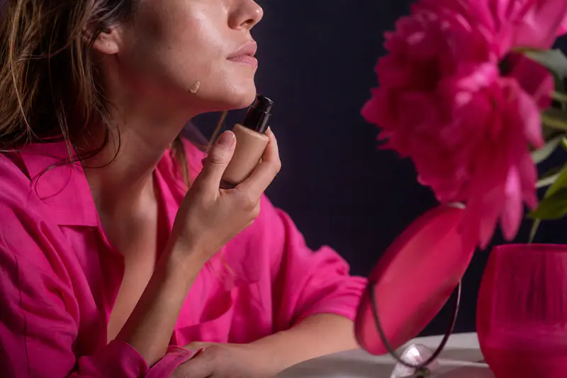 Femme testant une touche de fond de teint le long de la mâchoire, flacon à la main