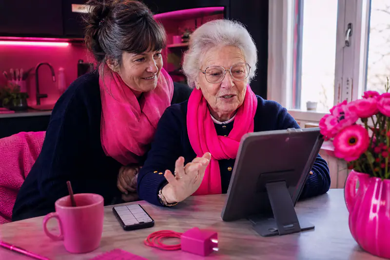 Une senior utilise une tablette simplifiée avec l'aide discrète de sa fille.