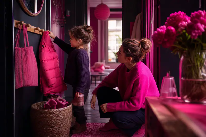 Jeune enfant rangeant seul son manteau dans une entrée aménagée à sa hauteur.