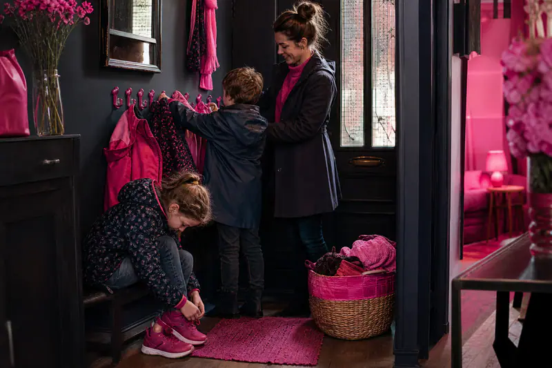 Deux enfants rangent manteaux et chaussures dans une entrée familiale automnale.