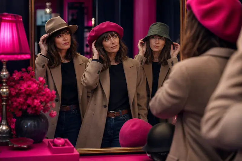 Femme essayant un fedora en feutre devant un miroir de chapellerie