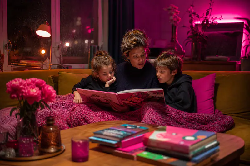 Une mère lit un album à deux enfants dans un salon d’automne.