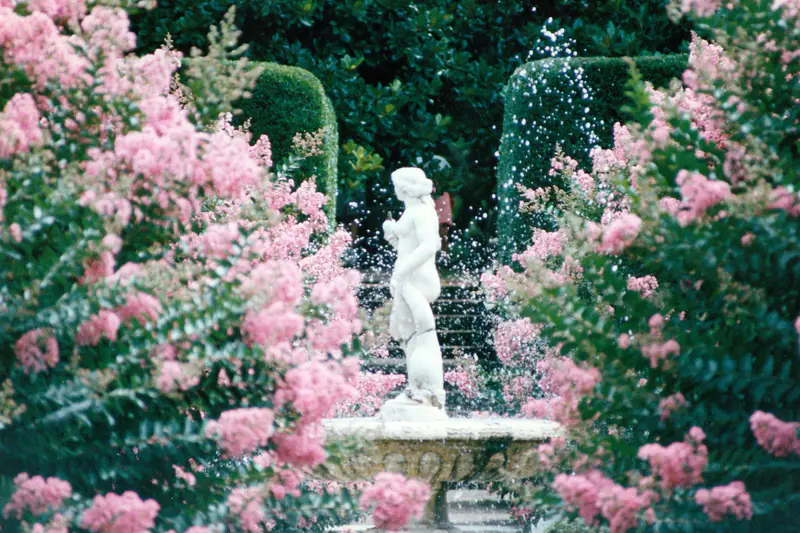 Fontaine en pierre entourée de graviers et vivaces dans un jardin d’automne