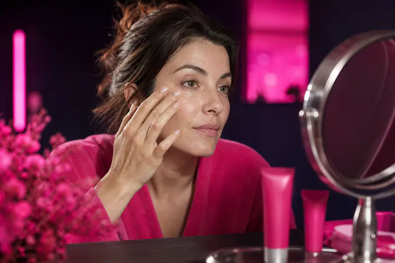 Femme appliquant délicatement une crème contour des yeux devant un miroir