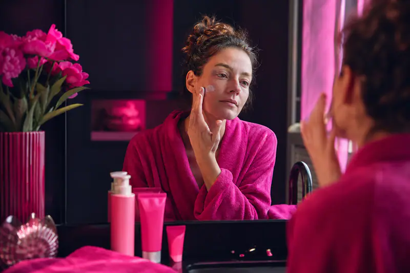 Femme appliquant une crème apaisante dans une salle de bains automnale.