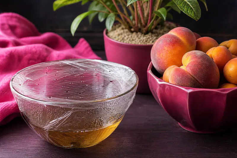 Bol de vinaigre couvert de film percé posé près d’une coupe de fruits mûrs