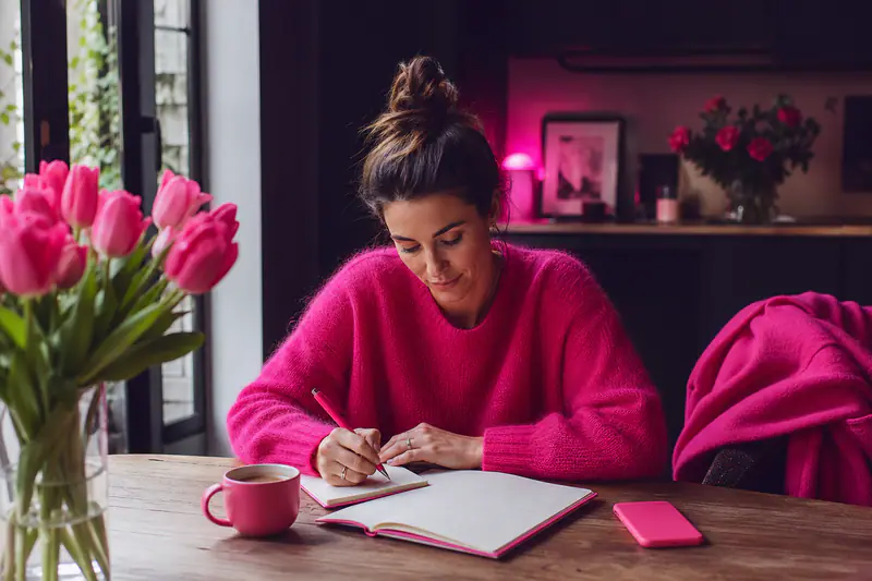 Femme écrivant ses priorités dans un carnet près d’un agenda printanier.