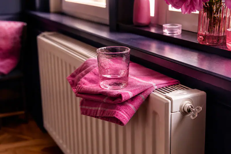 Clé de purge insérée dans la vis d’un radiateur blanc, chiffon et verre posés dessus