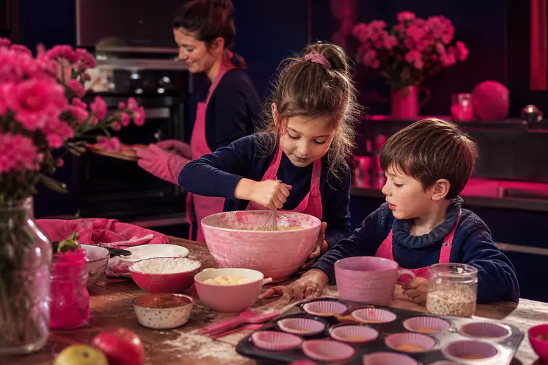 Deux enfants préparent des muffins aux pommes avec leur mère en cuisine.