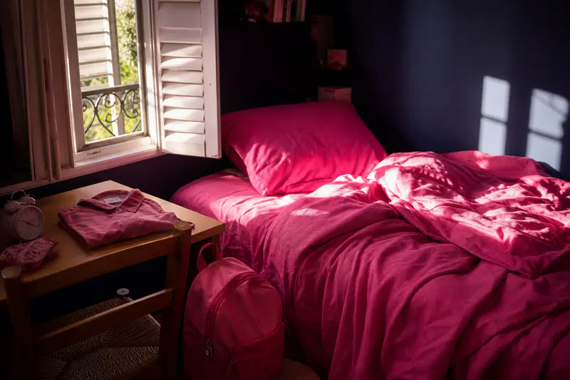 Chambre d’enfant au petit matin, volets ouverts sur la lumière, lit défait et sac à dos posé au sol