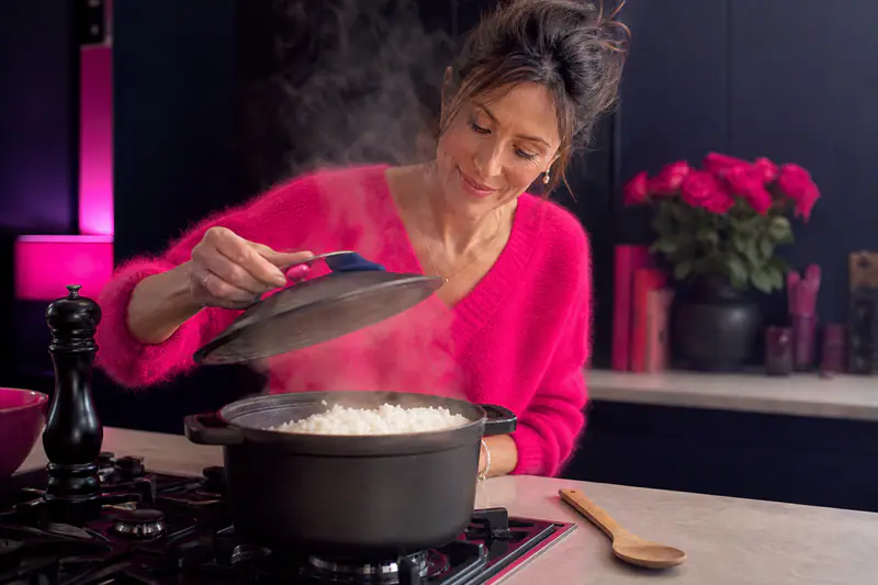 Femme soulevant le couvercle d’une casserole de riz fumant sur la cuisinière