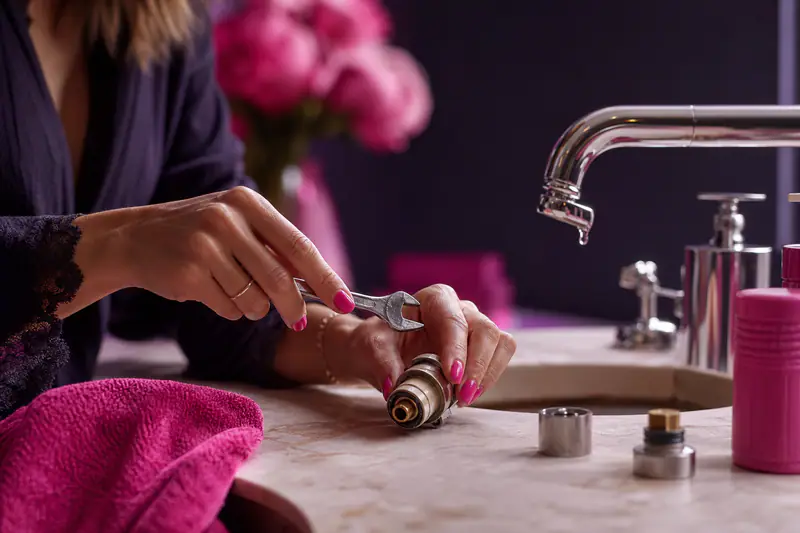 Mains démontant une cartouche de robinet avec une clé, goutte d’eau visible sur le bec
