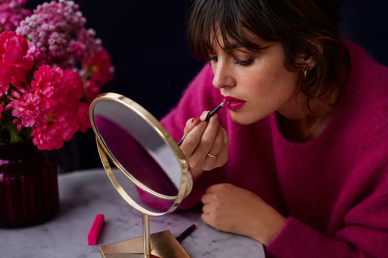 Femme appliquant un rouge à lèvres magenta au pinceau devant un miroir